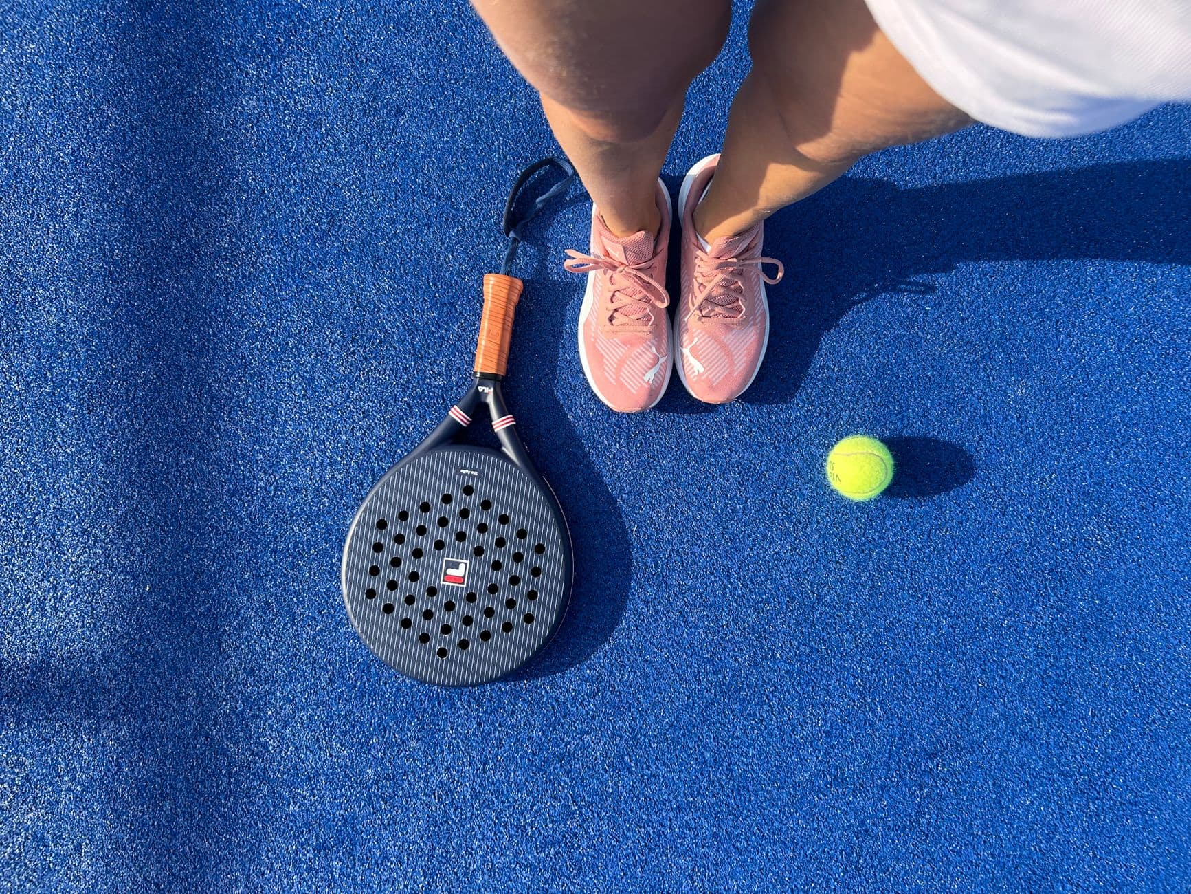 Padel-Spielerin von oben mit Schuhen, Schläger und Ball auf blauem Court
